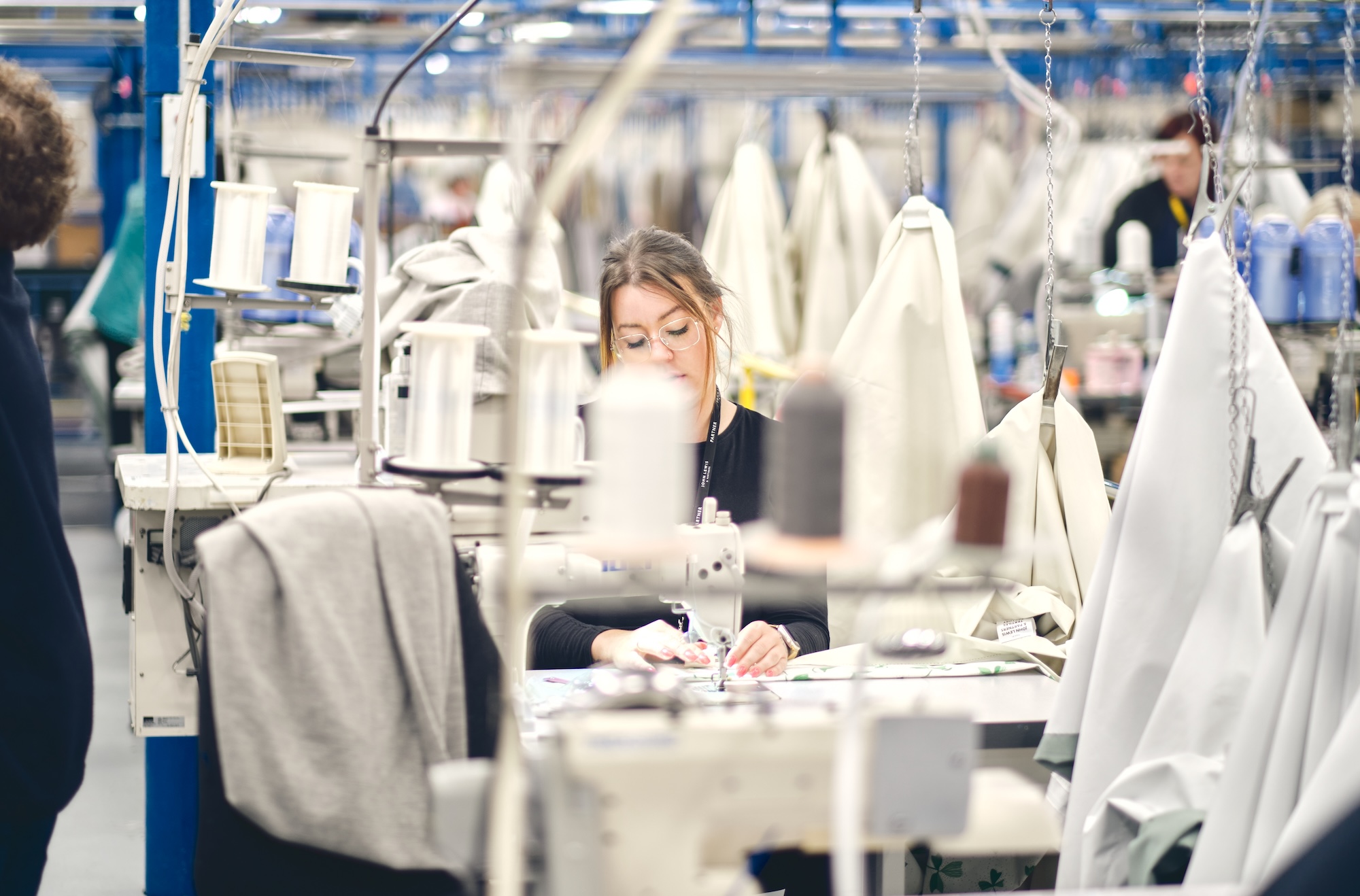 Professional textile worker operating industrial sewing machine in modern apparel manufacturing facility showcasing production operations